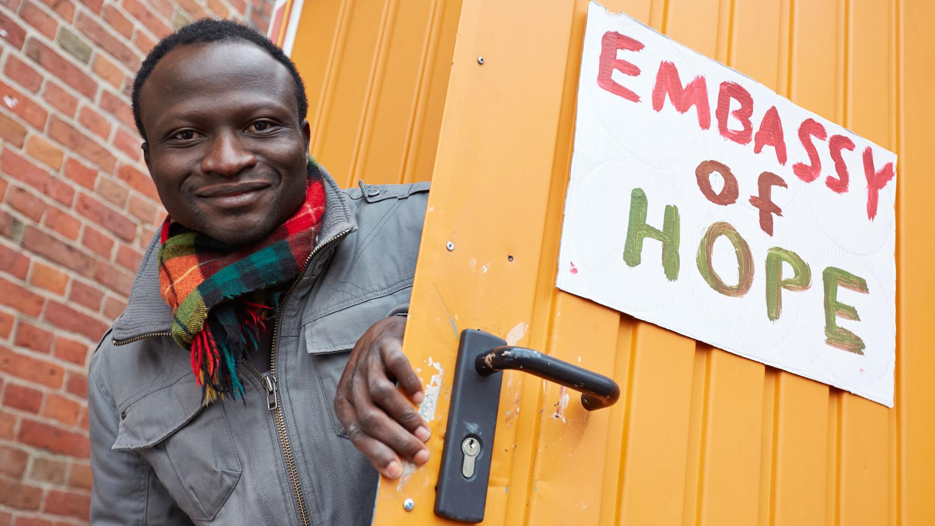 Der Ghanaer Andreas Listowell als Vertreter der "Lampedusa-Flüchtlinge" an der Tür eines Bauwagens mit der Aufschrift "Embassy of Hope". Der durch Spenden über Kiezhelden.com finanzierte Bauwagen soll den Flüchtlingen als Anlaufstelle und Treffpunkt dienen. Foto: Georg Wendt/dpa Der Ghanaer Andreas Listowell als Vertreter der "Lampedusa-Flüchtlinge" an der Tür eines Bauwagens mit der Aufschrift "Embassy of Hope". Der durch Spenden über Kiezhelden.com finanzierte Bauwagen soll den Flüchtlingen als Anlaufstelle und Treffpunkt dienen. Foto: Georg Wendt/dpa