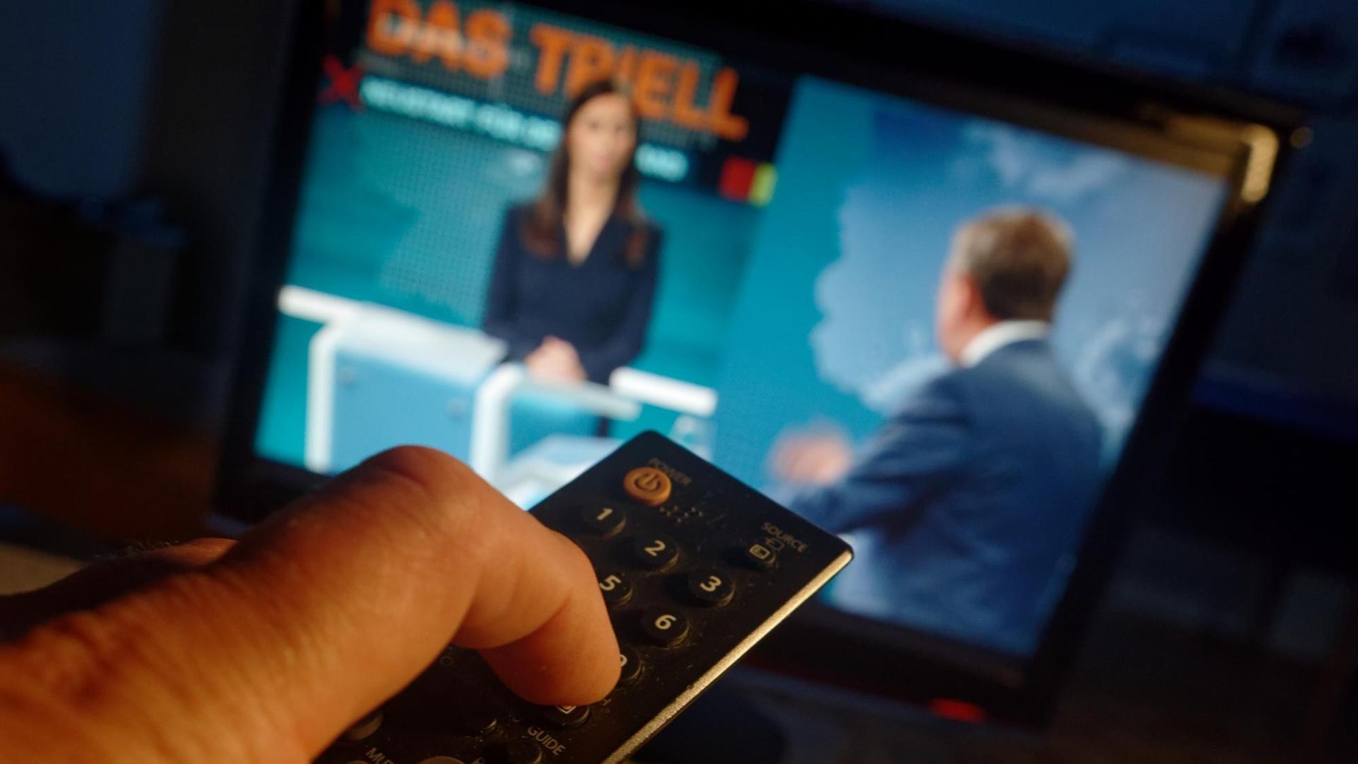Eine Hand drückt auf eine Fern-Bedienung, im Hintergrund ist ein Fernseher. Eine Hand drückt auf eine Fern-Bedienung, im Hintergrund ist ein Fernseher.