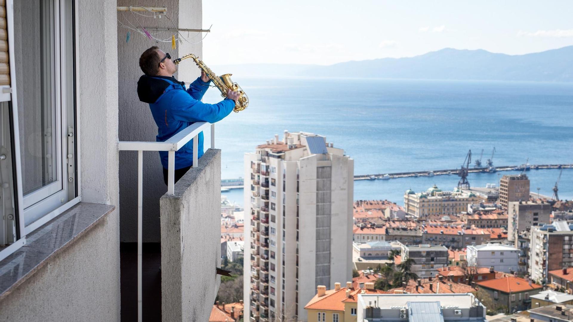 Ein Mann spielt Saxophon auf seinem Balkon und überblickt dabei die Hafenstadt von Rijeka in Kroatien.
