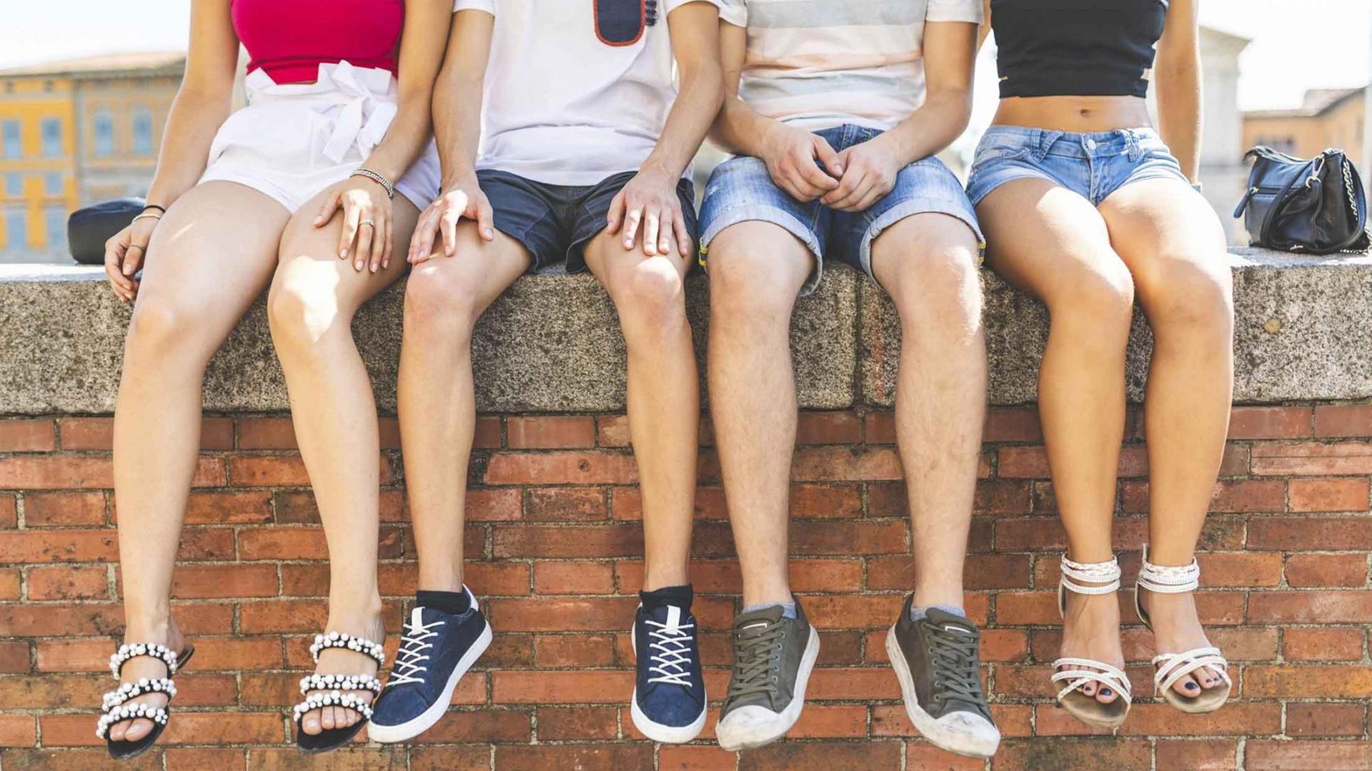 Vier Jugendliche sitzen auf einer Mauer und lassen die Füße baumeln. Vier Jugendliche sitzen auf einer Mauer und lassen die Füße baumeln.