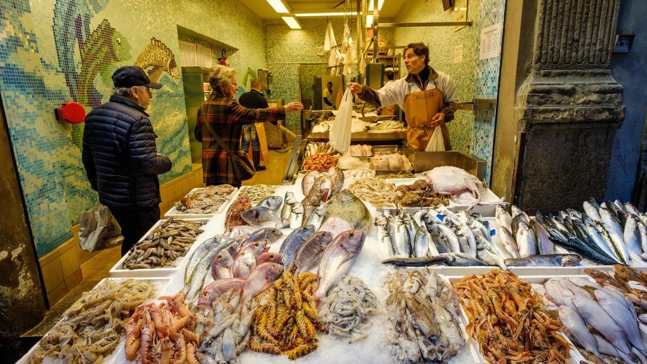 Das Bild zeigt ein Fischgeschäft in Bologna, Italien. In der Auslage liegt der Frischfisch, ein Verkäufer reicht einer Kundin eine Tüte. Das Bild zeigt ein Fischgeschäft in Bologna, Italien. In der Auslage liegt der Frischfisch, ein Verkäufer reicht einer Kundin eine Tüte.
