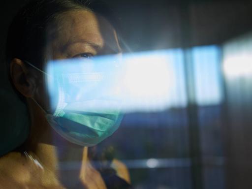 Eine Frau mit Mundschutz schaut durch eine Fensterscheibe