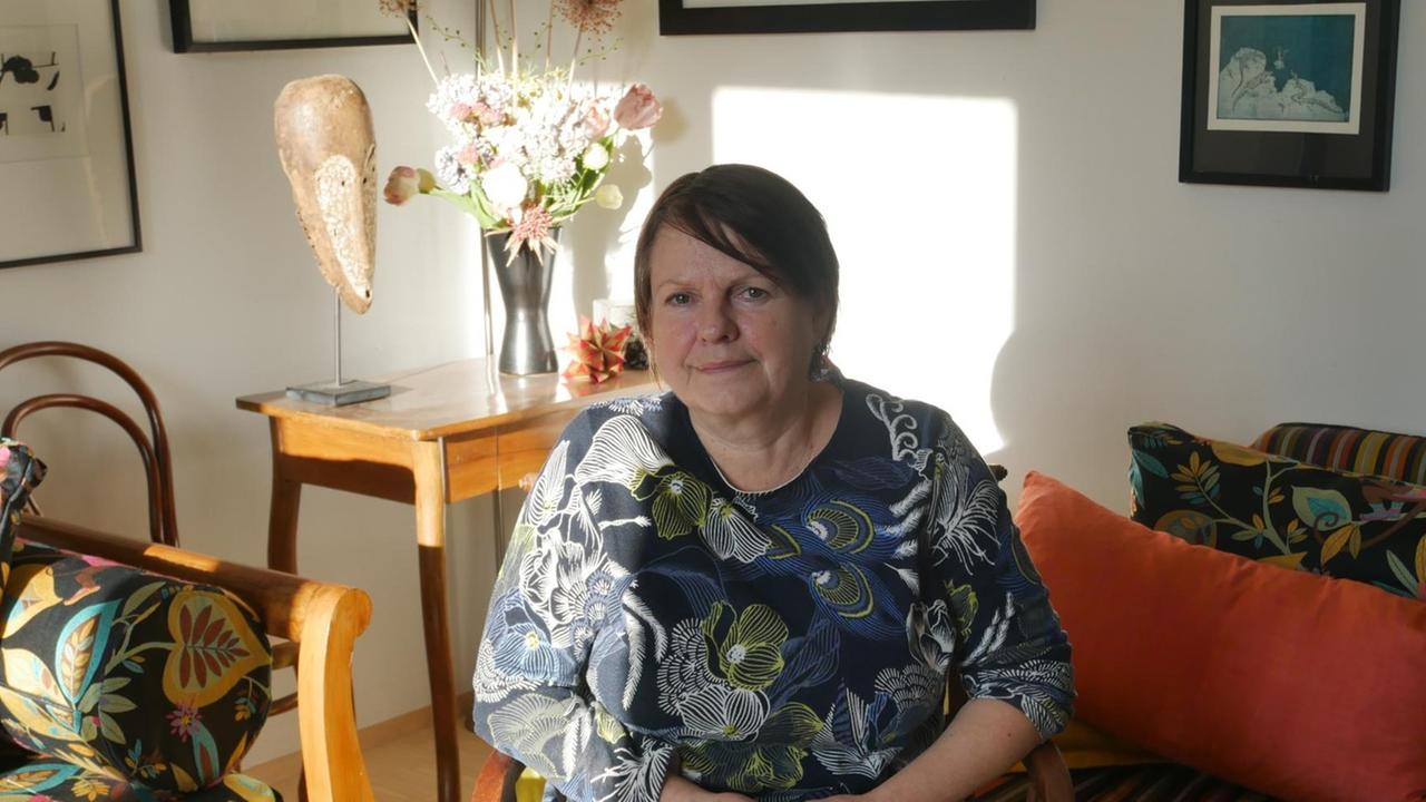 Die Kunsthistorikerin Simone Hain in einem Wohnzimmer mit geblümtem Sessel und gerahmten Bildern an den Wändern.