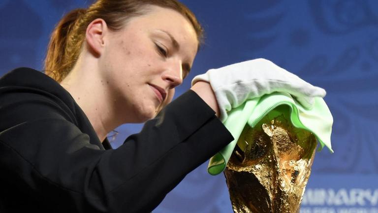 Eine Frau putzt am 24.07.2015 vor einer FIFA-Pressekonferenz im Konstantinpalast in St. Petersburg (Russland) den goldenen WM-Pokal.