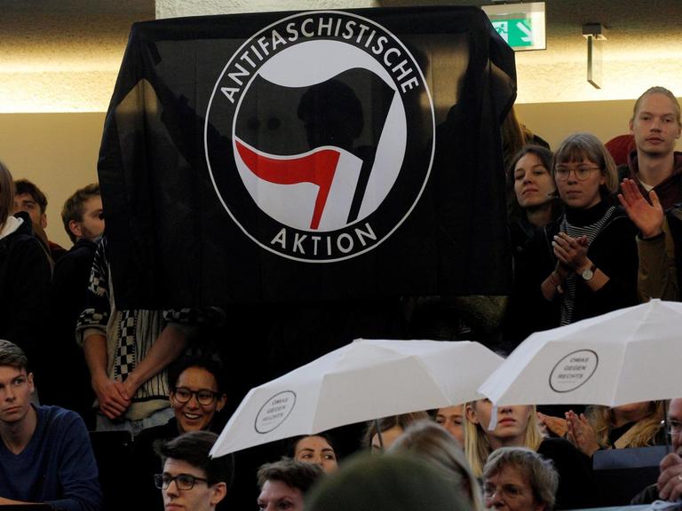Demonstrierende im Hörsaal halten eine Fahne hoch, auf der steht: Antifaschistische Aktion.