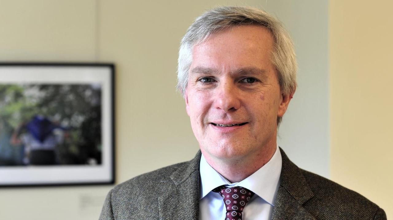 Professor Markus Rathey, im Büro, mit grauem Sakko, weißem Hemd und Krawatte, schaut freundlich lächelnd in die Kamera. Professor Markus Rathey, im Büro, mit grauem Sakko, weißem Hemd und Krawatte, schaut freundlich lächelnd in die Kamera.