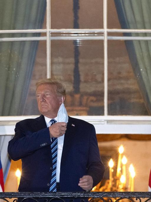 Präsident Trump steht auf dem Balkon am Weißen Haus und nimmt seine Schutzmaske ab