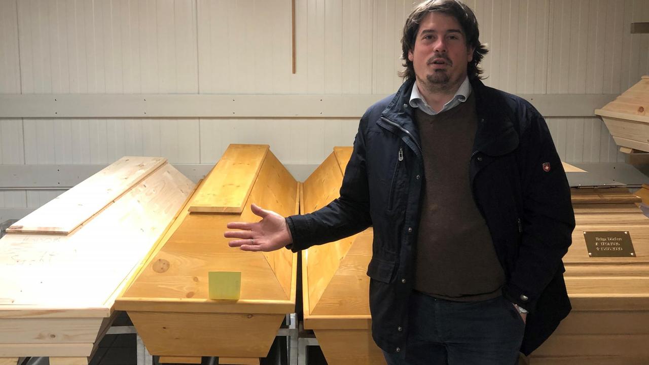 Der Friedhofsleiter steht vor geschlossenen Särgen in der Verstorbenenhalle. Der Friedhofsleiter steht vor geschlossenen Särgen in der Verstorbenenhalle.