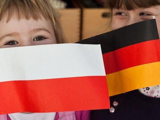 Zwei Kinder halten eine polnische und eine deutsche Fahnen in den Händen