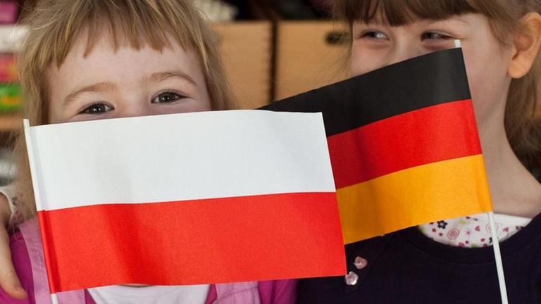 Zwei Kinder halten eine polnische und eine deutsche Fahnen in den Händen