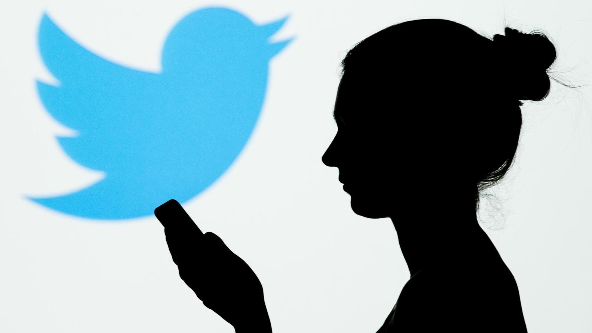 Silhouette einer Frau mit Mobiltelefon in der Hand, im Hintergrund das Vogel-Symbol von Twitter. Silhouette einer Frau mit Mobiltelefon in der Hand, im Hintergrund das Vogel-Symbol von Twitter.