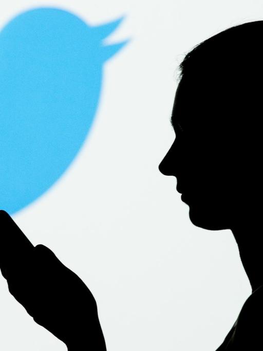 Silhouette einer Frau mit Mobiltelefon in der Hand, im Hintergrund das Vogel-Symbol von Twitter.