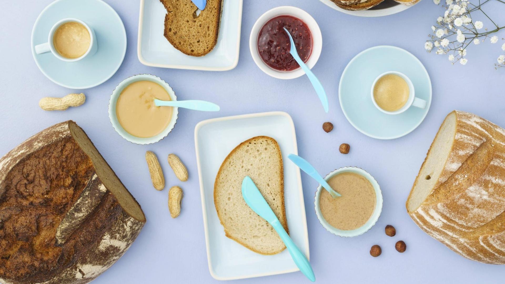 Frühstück auf einem hellen Tisch mit verschiedenen Brotsorten, Aufstrich und Erdnussbutter. Frühstück auf einem hellen Tisch mit verschiedenen Brotsorten, Aufstrich und Erdnussbutter.