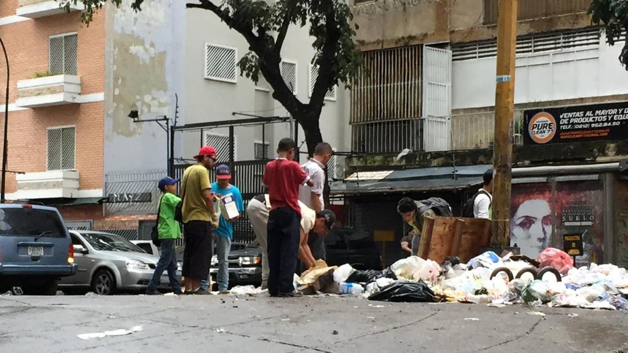 Auf einer Straße in Caracas wühlen junge Männer in Mülltüten. Auf einer Straße in Caracas wühlen junge Männer in Mülltüten.