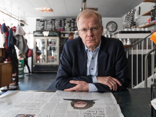 Der Lyriker Henning Ziebritzki sitzt in einem Café, vor sich auf dem Tisch eine aufgeschlagene Zeitung.