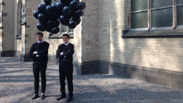 Das Bild zeigt Ludwig Abraham und Andy Ingamells schwarz gekleidet und jeweils mit einem Bund schwarzen Luftballons in der Hand. Die beiden stehen vor der St. Peter Kirche.