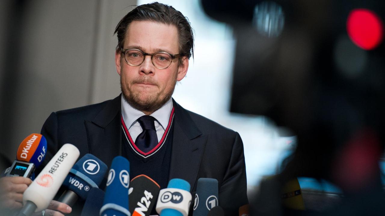 Ein Mann mit kurzen Haaren und Brille presst seine Lippen aufeinander – ihm sind viele Mikrofone und eine Kamera entgegen gestreckt. Ein Mann mit kurzen Haaren und Brille presst seine Lippen aufeinander – ihm sind viele Mikrofone und eine Kamera entgegen gestreckt.