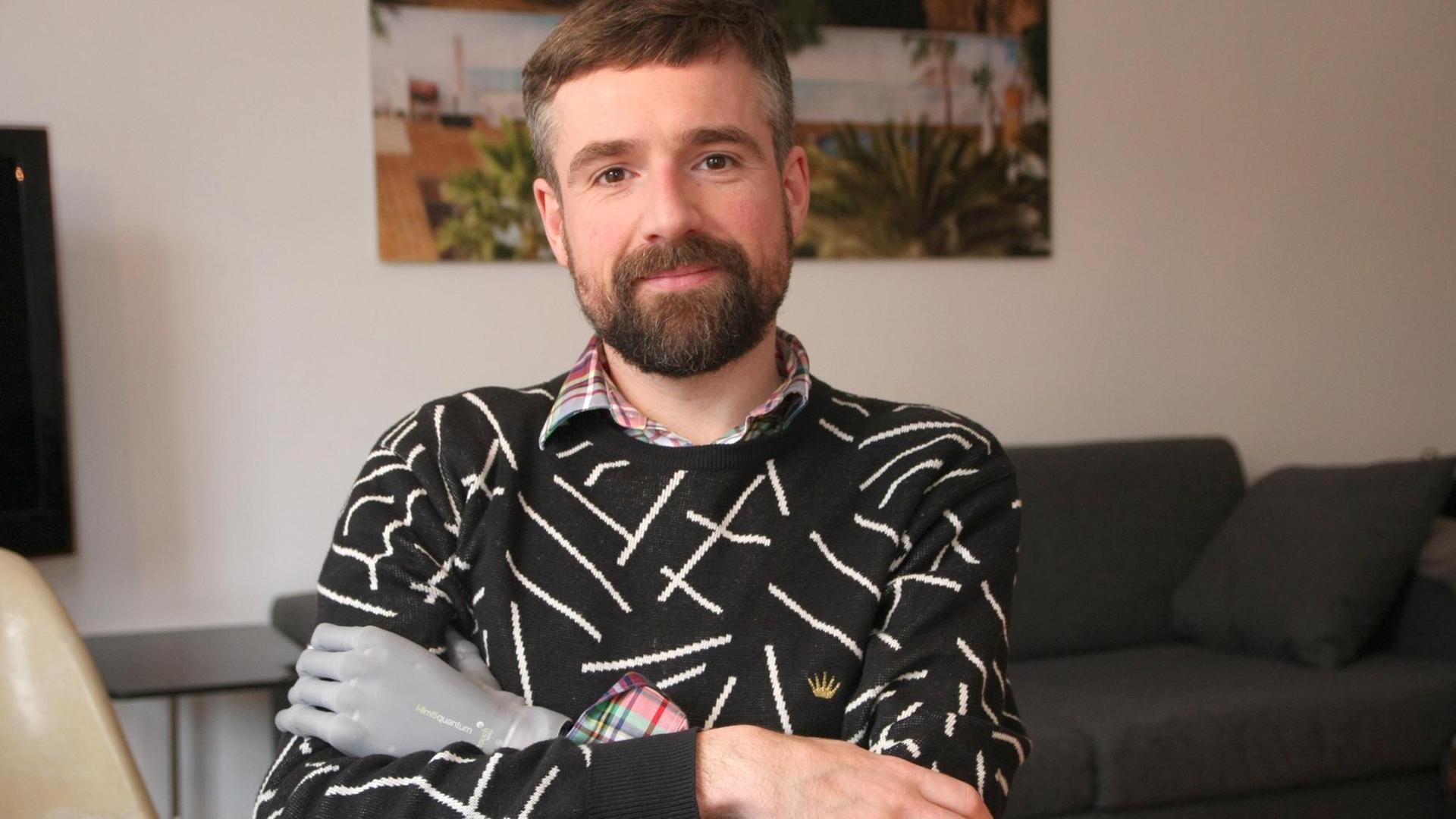Der Psychologe Bertolt Meyer im schwarz-weiß-gemusterten Pullover in einer Porträtaufnahme. Er hat die Arme vor dem Körper verschränkt, sein graue Unterarmprothese ist am linken Arm deutlich zu sehen. Der Psychologe Bertolt Meyer im schwarz-weiß-gemusterten Pullover in einer Porträtaufnahme. Er hat die Arme vor dem Körper verschränkt, sein graue Unterarmprothese ist am linken Arm deutlich zu sehen.