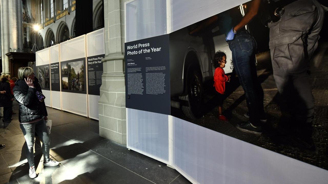 Das Bild "Crying Girl on the Border" von US-Fotograf John Moore: Besucher*innen blicken auf das Foto des Jahres 2019 bei der Ausstellung zum World Press Photo in Amsterdam. Die Nachtaufnahme ziegt ein weinendes kleines Mädchen, das vor den riesigen Radkappen eines Pick-ups der US-Grenzpolizei steht. Seine Mutter muss sich an den Wagen lehnen und wird von Beamten durchsucht. Das Bild "Crying Girl on the Border" von US-Fotograf John Moore: Besucher*innen blicken auf das Foto des Jahres 2019 bei der Ausstellung zum World Press Photo in Amsterdam. Die Nachtaufnahme ziegt ein weinendes kleines Mädchen, das vor den riesigen Radkappen eines Pick-ups der US-Grenzpolizei steht. Seine Mutter muss sich an den Wagen lehnen und wird von Beamten durchsucht.