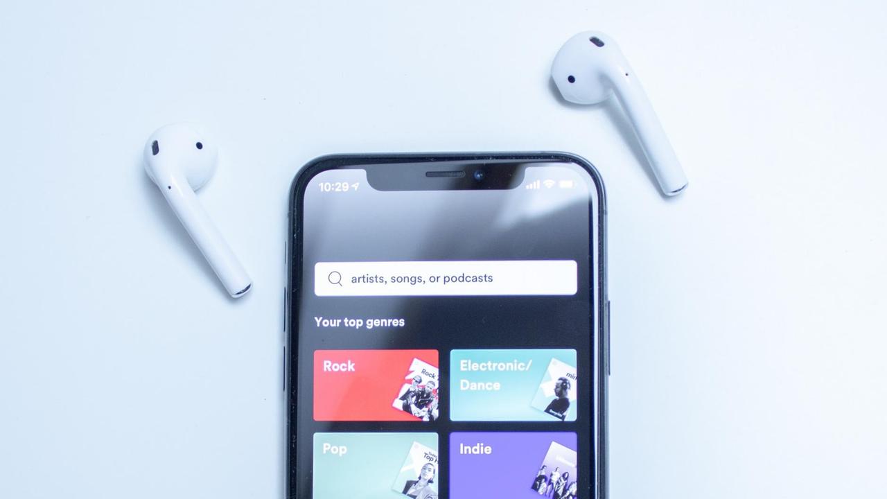 Eine Sachaufnahme zeigt ein Mobiltelefon mit der Spotify-App und moderen Bluetooth-Kopfhörern. Eine Sachaufnahme zeigt ein Mobiltelefon mit der Spotify-App und moderen Bluetooth-Kopfhörern.