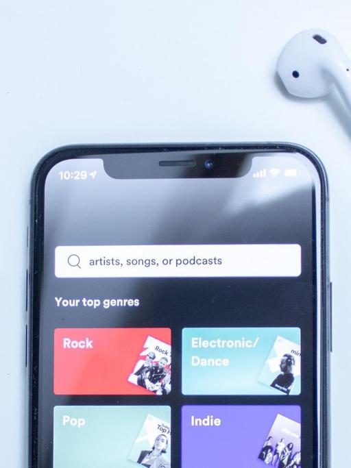Eine Sachaufnahme zeigt ein Mobiltelefon mit der Spotify-App und moderen Bluetooth-Kopfhörern.
