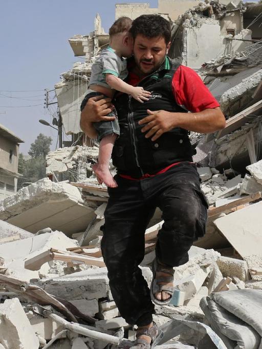 Ein Mann trägt sein Kind in Aleppo am Samstag, 24.09.2016, aus den Trümmern eines zerstörten Gebäudes.