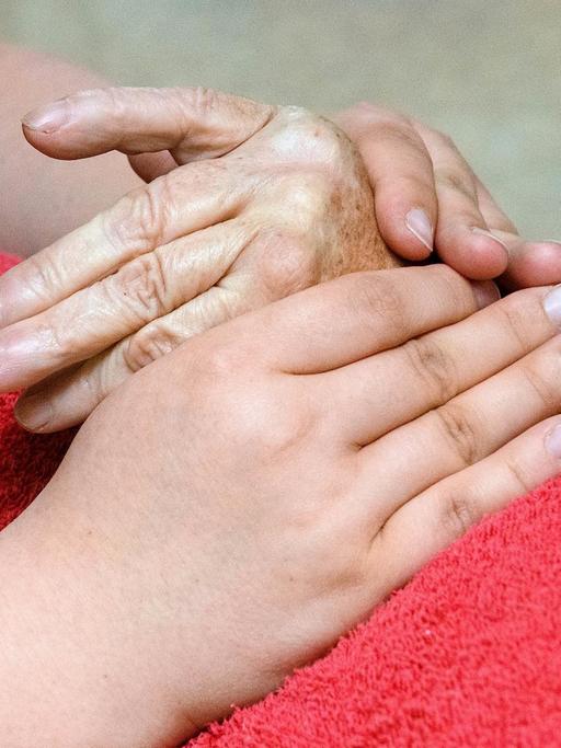 Hände einer an Arthritis erkrankten Patientin werden von einer Ergotherapeutin massiert. Die Massage der Hände wärmt und mobilisiert die entzuendeten Gelenke der Hand.