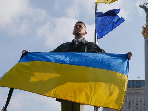 Ein Ukrainer hält in Kiew die Nationalflagge in die Höhe.