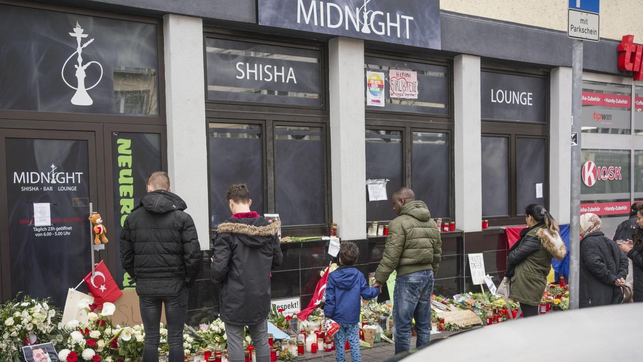 Hanau: Menschen stehen an einem der Tatorte vor einer Shisha-Bar am Heumarkt, wo Bürger mit Blumen, Plakaten und Kerzen ihre Trauer zum Ausdruck bringen. Am 19.02.2020 hatte ein 43-jähriger Deutscher bei einem mutmaßlich rassistischen Anschlag mehrere Menschen und sich selbst erschossen.