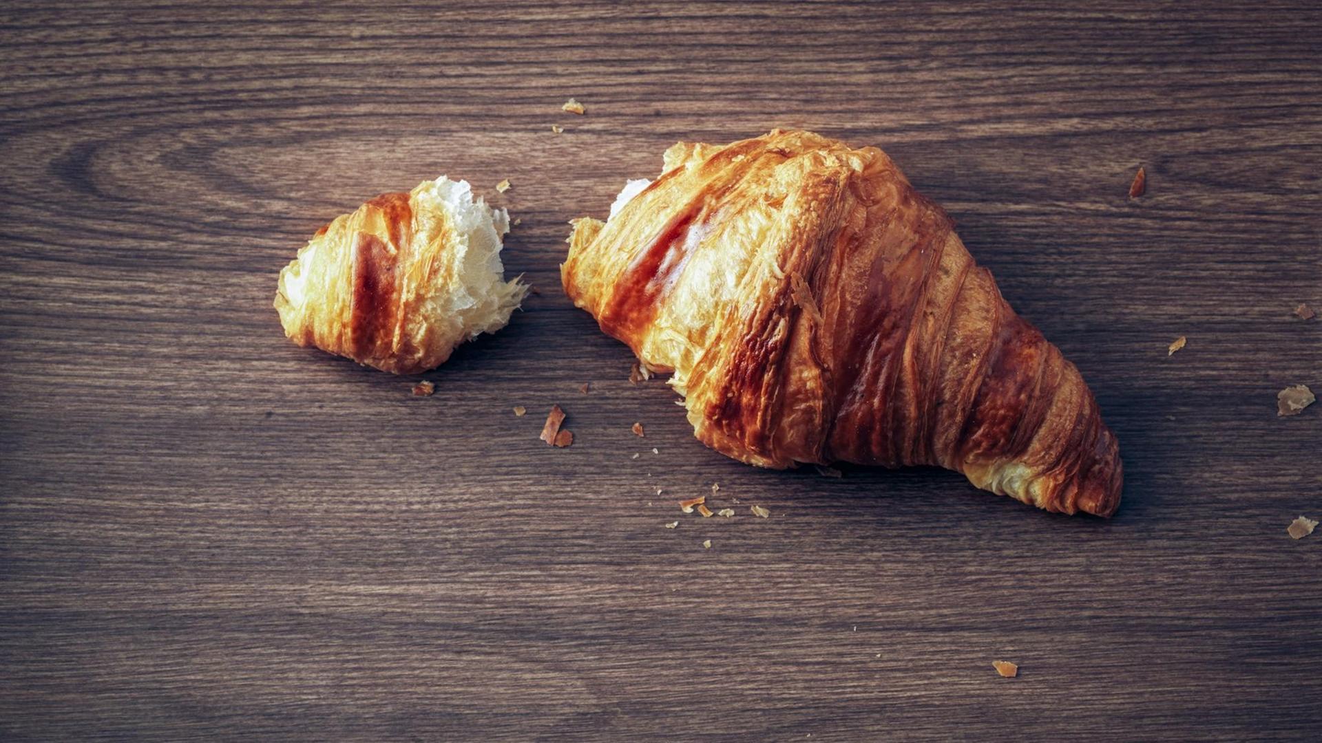 Ein Croissant liegt auf einem dunklen Holztisch Ein Croissant liegt auf einem dunklen Holztisch
