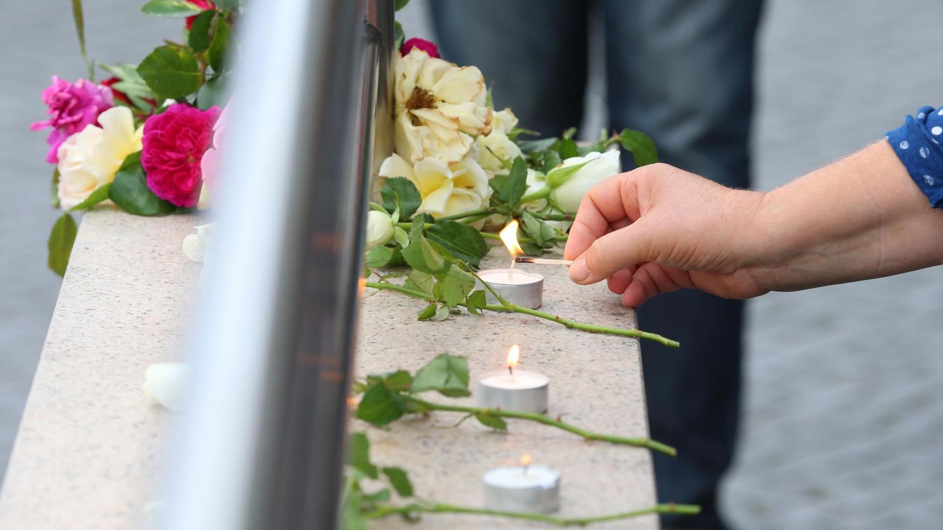 Eine Hand legt eine Blume auf einer Mauer neben Kerzen nieder. Eine Hand legt eine Blume auf einer Mauer neben Kerzen nieder.