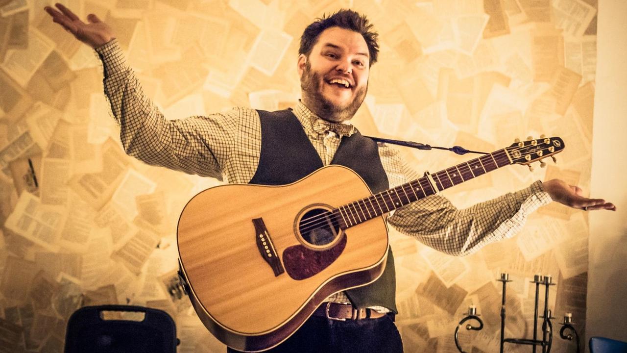 Der isländische Musiker Svavar Knutur mit Gitarre um den Hals breitet lachend seine Arme aus Der isländische Musiker Svavar Knutur mit Gitarre um den Hals breitet lachend seine Arme aus