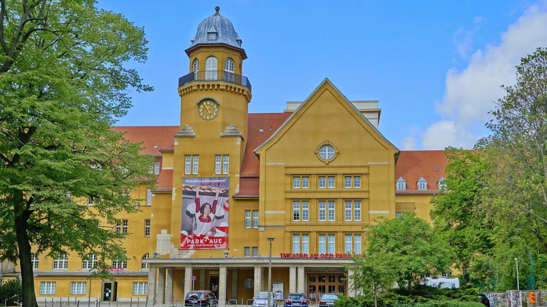 Außenansicht des Theaters an der Parkaue in Berlin-Lichtenberg. Ein großes Gebäude mit gelber Fassade, einem Spitzdach und einem kleinen Türmchen. Außenansicht des Theaters an der Parkaue in Berlin-Lichtenberg. Ein großes Gebäude mit gelber Fassade, einem Spitzdach und einem kleinen Türmchen.