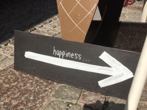 Ein Pappschild mit einem Pfeil nach rechts auf dem steht "happiness"