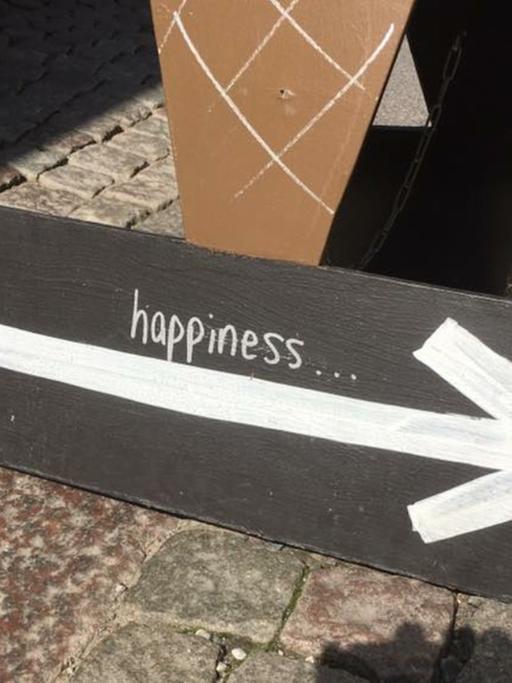 Ein Pappschild mit einem Pfeil nach rechts auf dem steht "happiness"
