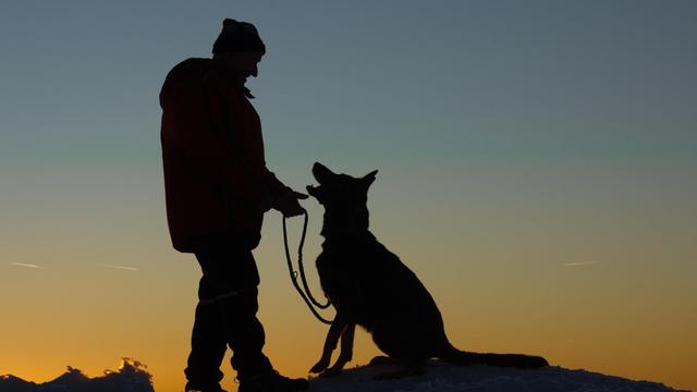 Ein Mann mit Hund im Schnee bei Sonnenuntergang.