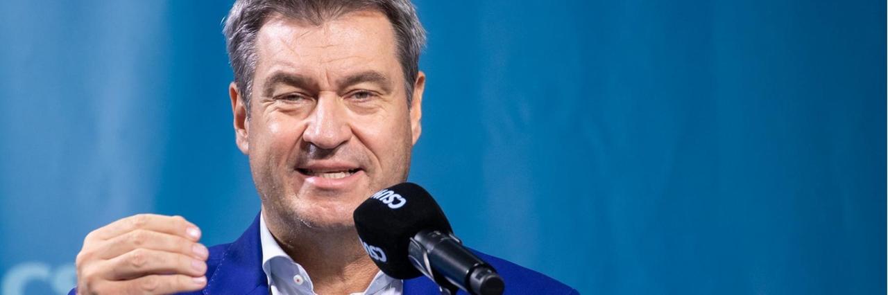 Markus Söder spricht in ein Mikrofon auf einer Bühne Markus Söder spricht in ein Mikrofon auf einer Bühne