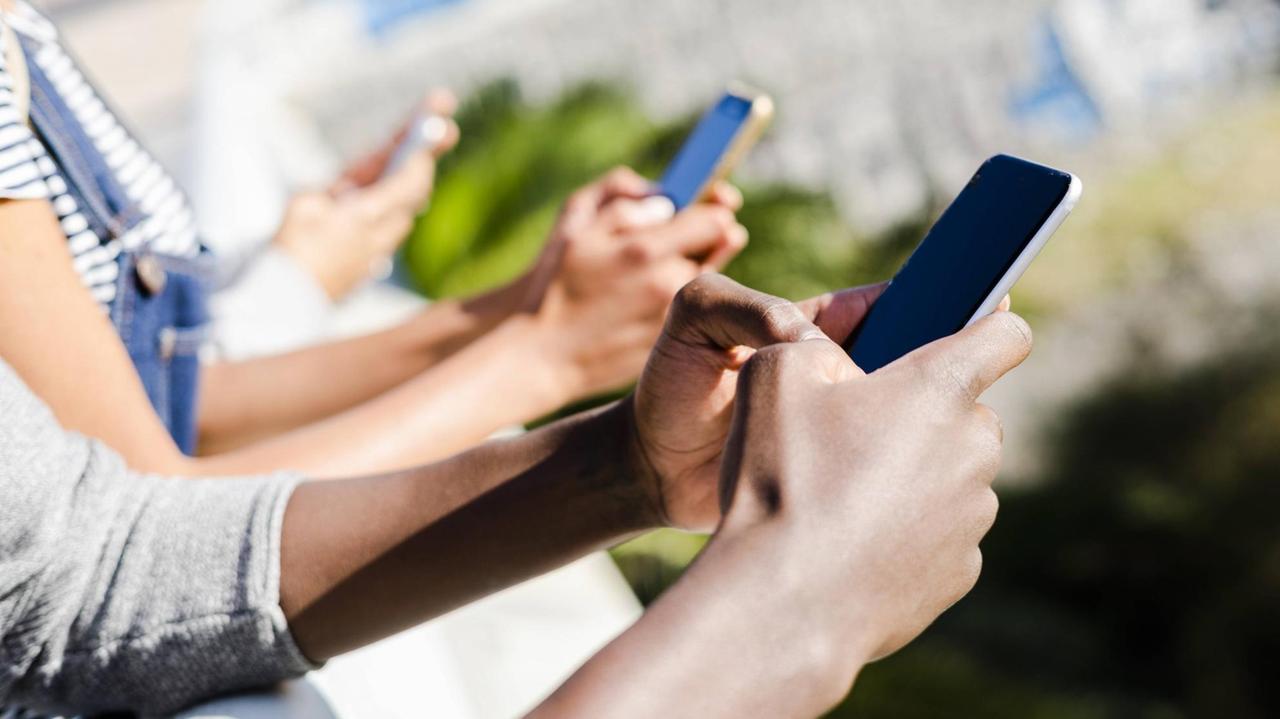 Symbolfoto: Menschen sitzen zusammen und halten jeweils ein Smartphone in der Hand. Symbolfoto: Menschen sitzen zusammen und halten jeweils ein Smartphone in der Hand.