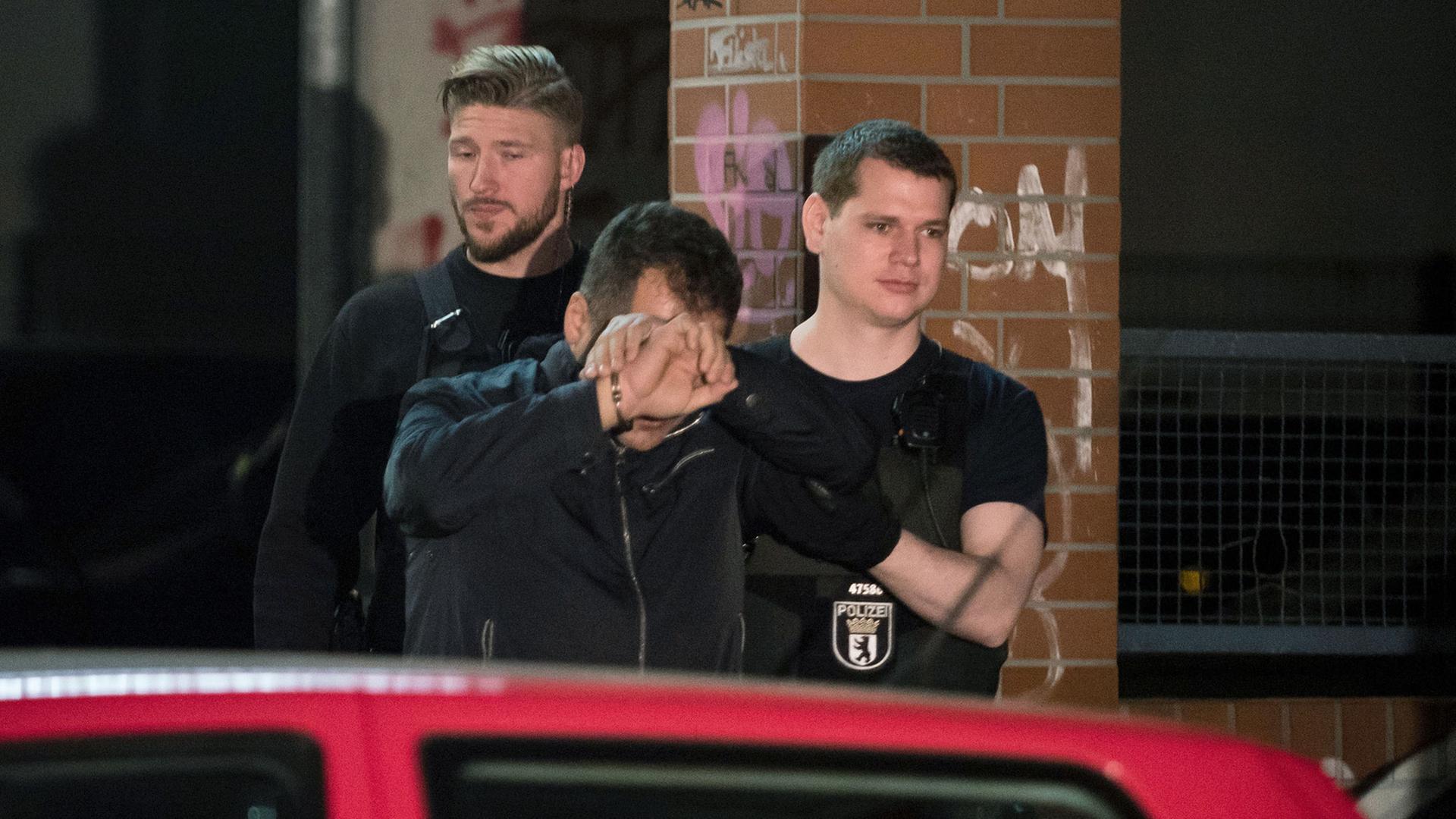 Polizisten führen bei einem Einsatz eine Person in Handschellen aus einem Haus in Berlin im Bezirk Neukölln. Polizisten führen bei einem Einsatz eine Person in Handschellen aus einem Haus in Berlin im Bezirk Neukölln.