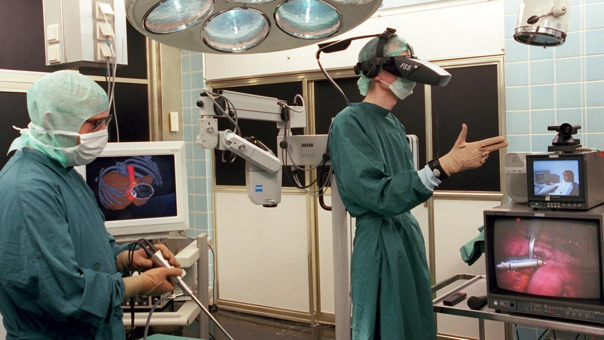 Im "OP 2000", dem Operationssaal der Zukunft, überprüft ein Mitarbeiter des Forschungsprojekts Surgical Research Unit OP 2000 in der Robert-Rössle-Klinik am Max-Delbrück-Centrum des Universitätsklinikums Charite, Berlin, ein stereoskopisches Laparoskop (links) für die minimal-invasive Chirurgie. Auf Monitoren sind stereoskopische Aufnahmen zur Operationsplanung dargestellt , andere Bildschirme (vorn rechts) werden für intraoperative Telekonferenzen eingesetzt, zu denen verschiedene externe Experten live zugeschaltet werden können. Mit Head-mounted-Display (Datenhelm) und Cyberglove (Datenhandschuh) ist zusätzlich ein klassisches Virtual Reality (VR-)-Szenario dargestellt. Das Projekt OP 2000 dient der weiteren Verbesserung der Tumordiagnostik und -therapie, der Ausbildung und dem Training der Mediziner. Im "OP 2000", dem Operationssaal der Zukunft, überprüft ein Mitarbeiter des Forschungsprojekts Surgical Research Unit OP 2000 in der Robert-Rössle-Klinik am Max-Delbrück-Centrum des Universitätsklinikums Charite, Berlin, ein stereoskopisches Laparoskop (links) für die minimal-invasive Chirurgie. Auf Monitoren sind stereoskopische Aufnahmen zur Operationsplanung dargestellt , andere Bildschirme (vorn rechts) werden für intraoperative Telekonferenzen eingesetzt, zu denen verschiedene externe Experten live zugeschaltet werden können. Mit Head-mounted-Display (Datenhelm) und Cyberglove (Datenhandschuh) ist zusätzlich ein klassisches Virtual Reality (VR-)-Szenario dargestellt. Das Projekt OP 2000 dient der weiteren Verbesserung der Tumordiagnostik und -therapie, der Ausbildung und dem Training der Mediziner.