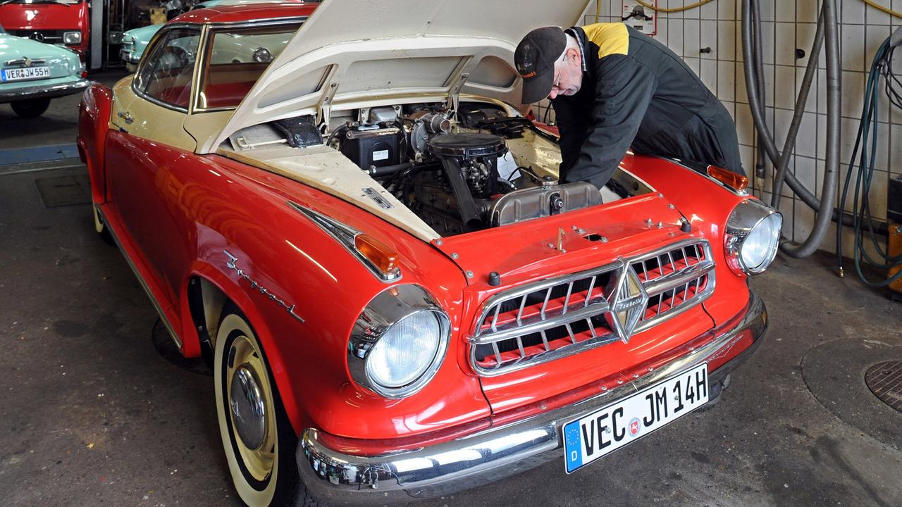 Ein Mechaniker repariert den Motor eines roten Oldtimers.