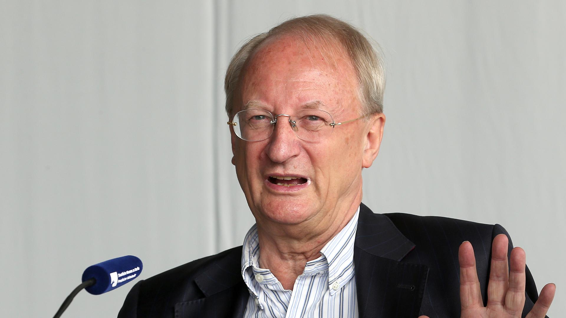 Klaus Staeck sitzt vor einem Mikrofon und hebt die Hand Klaus Staeck sitzt vor einem Mikrofon und hebt die Hand
