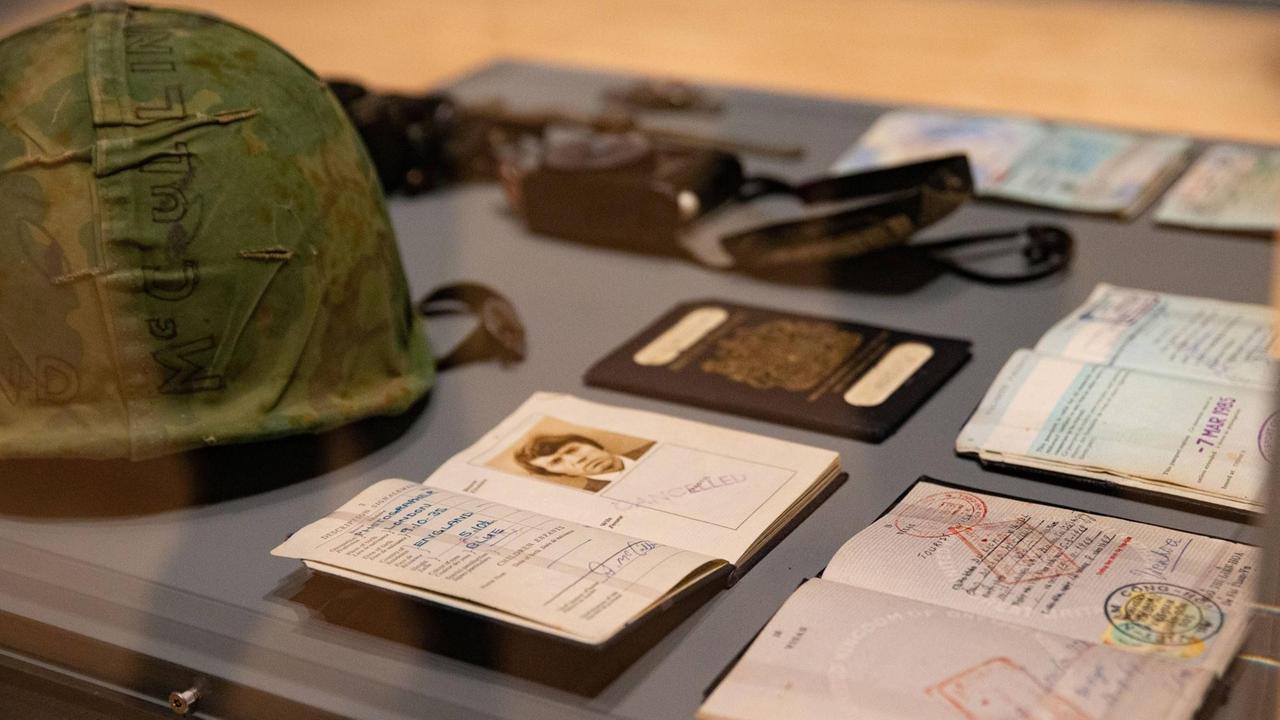 In einem Schaufenster liegen mehrere Dokumente, wie Reisepässe, ein Schutzhelm sowie eine Fotokamera. In einem Schaufenster liegen mehrere Dokumente, wie Reisepässe, ein Schutzhelm sowie eine Fotokamera.