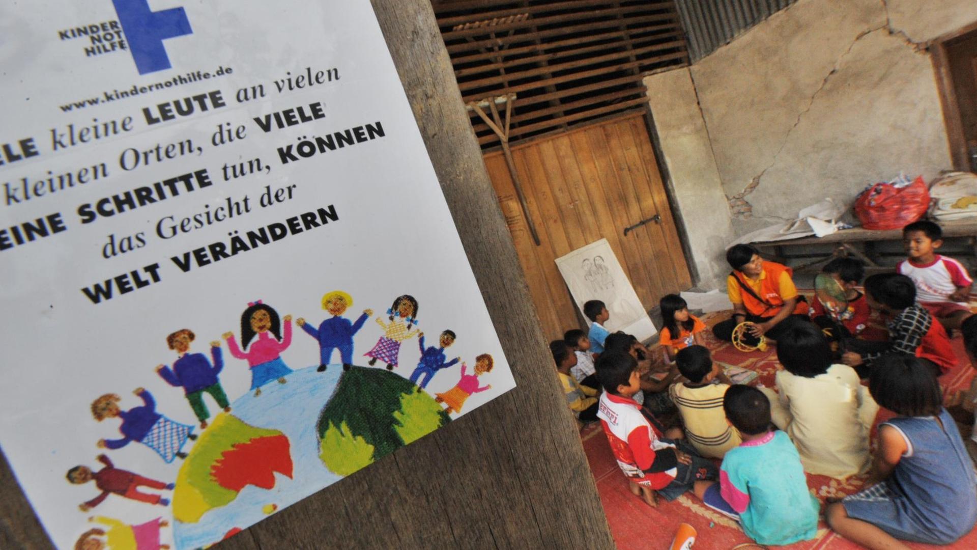 To go with Indonesia-quake-aid-children by Aubrey Belford In a picture taken on October 8, 2009 a poster for German-based Christian charitable organisation Kindernothilfe adorns the wall as a volunteer plays games with the children of Pasadama village in Pariaman following the recent 7.6-magnitude earthquake that struck the western coast of the island. Many child survivors of the huge earthquake on Sumatra island on September 30 have been left traumatised by a disaster that the United Nations says killed upwards of 1,100 people. As international aid pours in and authorities clean up buildings shattered in the quake, a small number of relief groups are working to repair widespread shock before it sets in and becomes lasting psychological damage. AFP PHOTO / BAY ISMOYO (Photo by BAY ISMOYO / AFP)