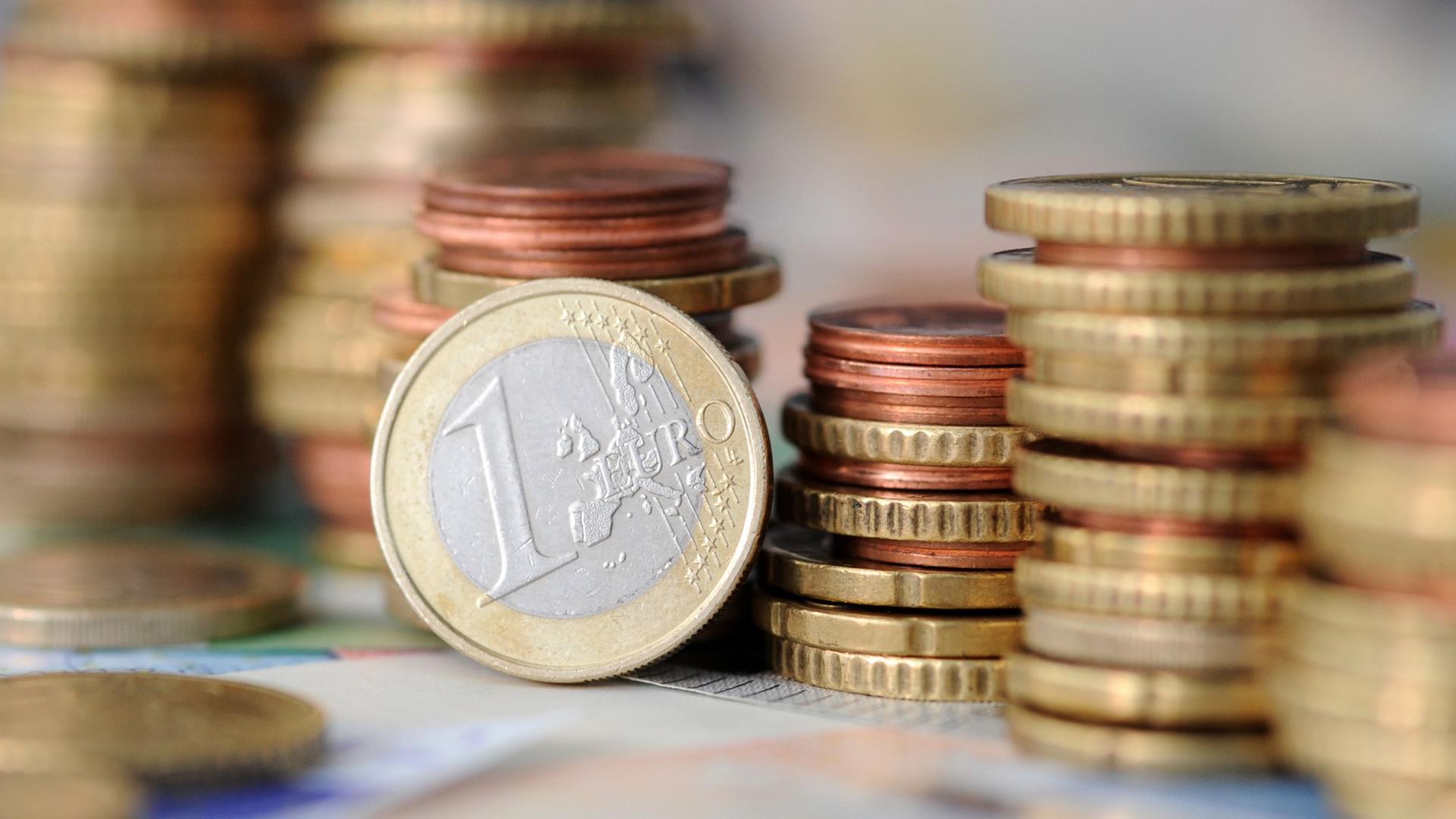 Eine Ein-Euro-Münze und einige Stapel von verschiedenen anderen Münzen Eine Ein-Euro-Münze und einige Stapel von verschiedenen anderen Münzen