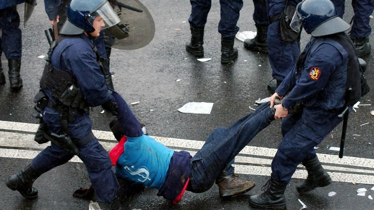 Gepanzerte Polizisten tragen einen Demonstranten von der Straße. Gepanzerte Polizisten tragen einen Demonstranten von der Straße.