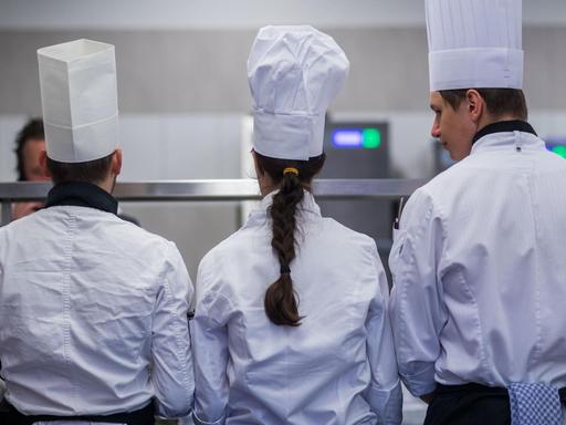 Drei junge Köche bei den Landesmeisterschaften des Gastro-Nachwuchses in Mecklenburg-Vorpommern stehen von der Kamera abgewandt und arbeiten an ihren Speisen.
