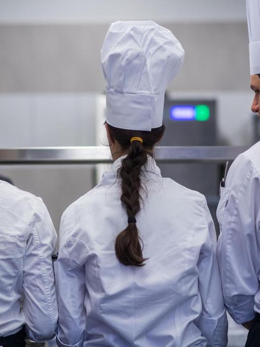 Drei junge Köche bei den Landesmeisterschaften des Gastro-Nachwuchses in Mecklenburg-Vorpommern stehen von der Kamera abgewandt und arbeiten an ihren Speisen.