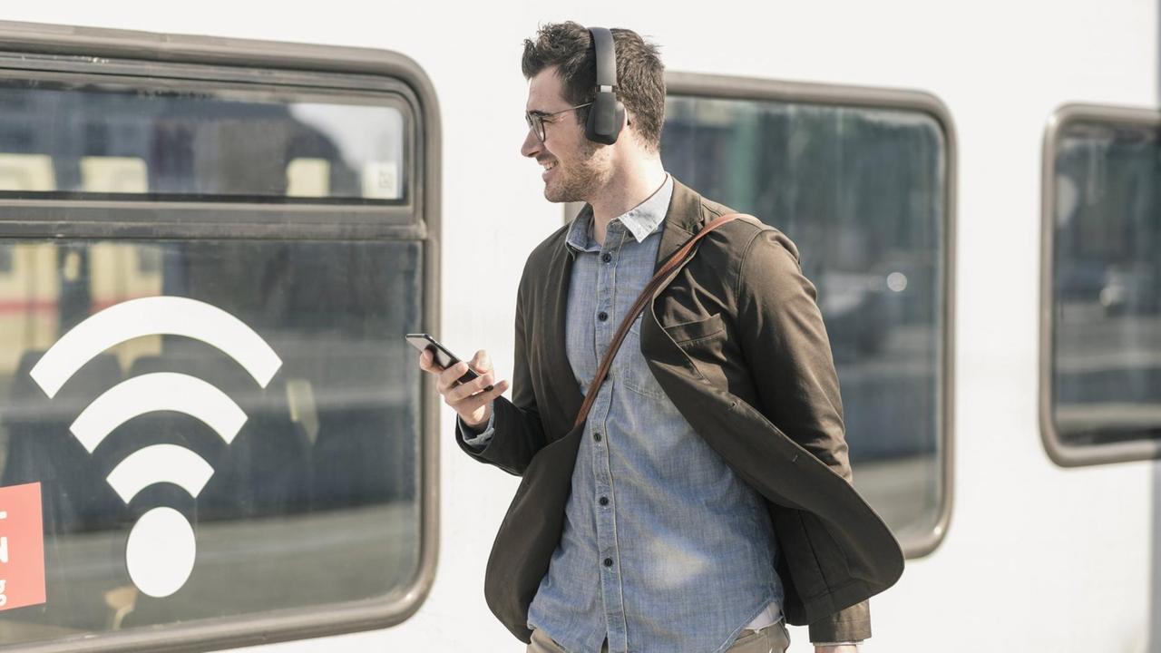 Mann mit Kopfhörern und Handy vor Zug Mann mit Kopfhörern und Handy vor Zug