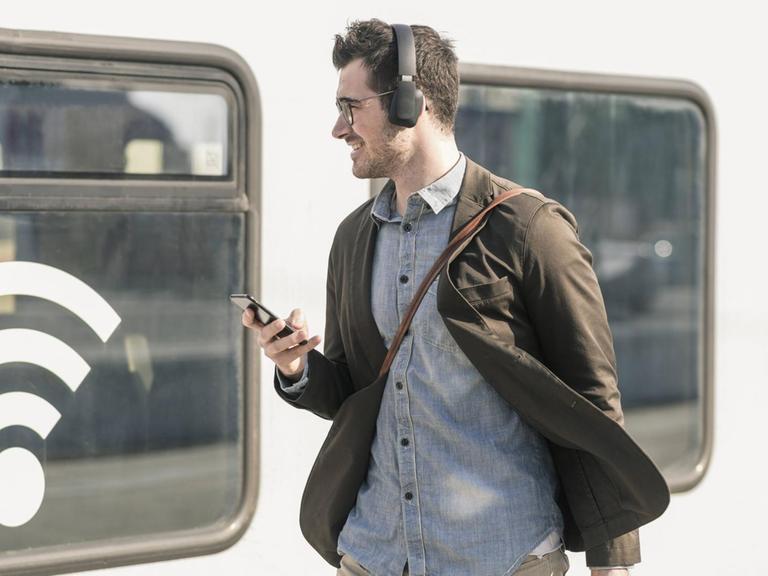 Mann mit Kopfhörern und Handy vor Zug